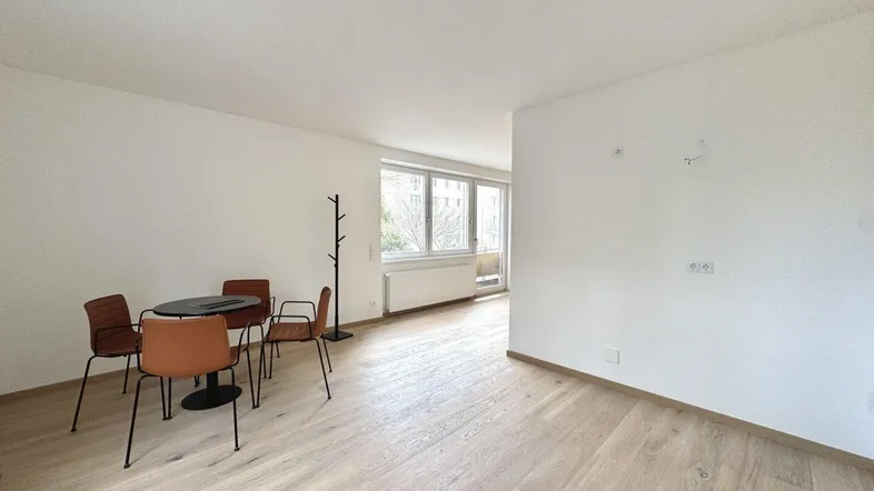Heller, offener Wohnbereich mit Parkettboden und einem kleinen Essbereich am Fenster.