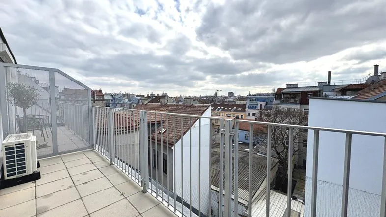 Geräumige Dachterrasse mit Stadtblick, moderner Metallbrüstung und Klimaanlage unter bewölktem Himmel.