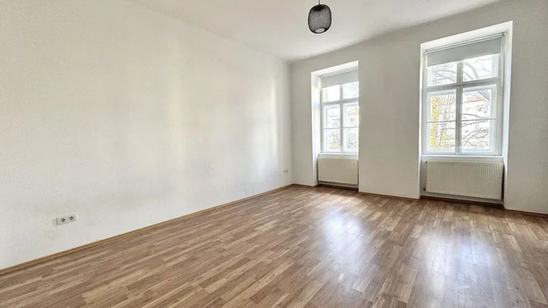 Helles Zimmer mit Laminatboden und zwei Fenstern, bereit zur individuellen Gestaltung.