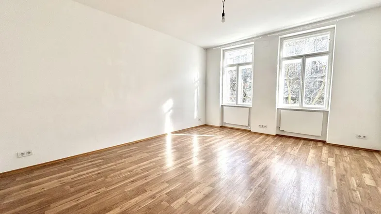 Helles Zimmer mit Holzboden und zwei großen Fenstern, ideal als Wohn- oder Schlafzimmer.