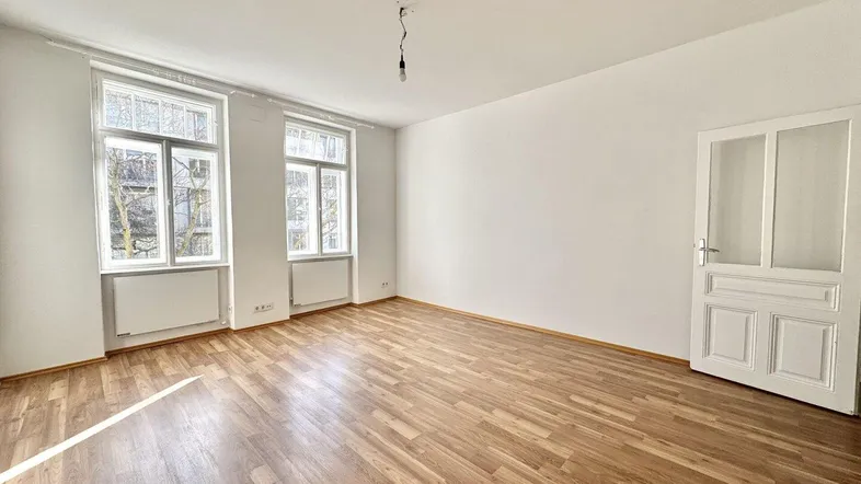 Geräumiges Zimmer mit Holzboden, zwei großen Fenstern und viel Tageslicht.