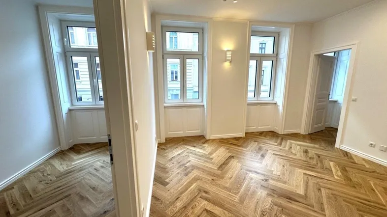 Helles Wohnzimmer mit elegantem Fischgrätparkettboden und mehreren hohen Fenstern, die viel Tageslicht hereinlassen.