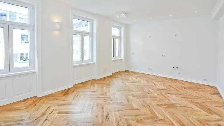 Helles, leeres Zimmer mit Fischgrätparkett und mehreren Fenstern, bereit zur individuellen Gestaltung.