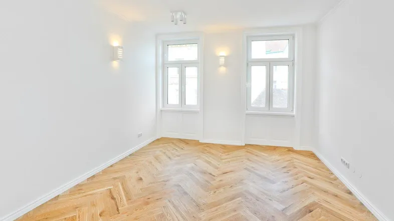 Helles Zimmer mit frisch verlegtem Fischgrätparkett und zwei großen Fenstern.