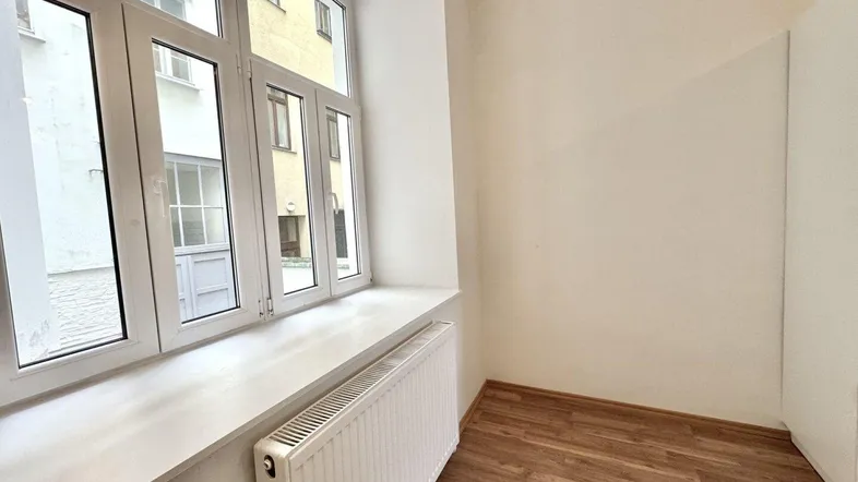Kleiner Raum mit Fenster zum Innenhof, Heizkörper und Holzboden.