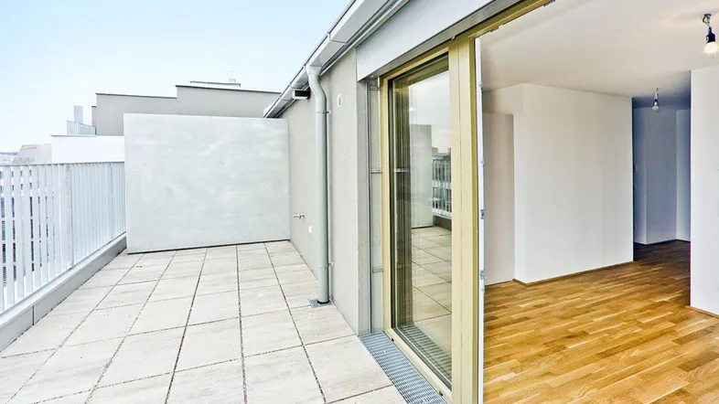 Geräumige Dachterrasse mit hellen Fliesen und Zugang zu einem modernen Innenraum.