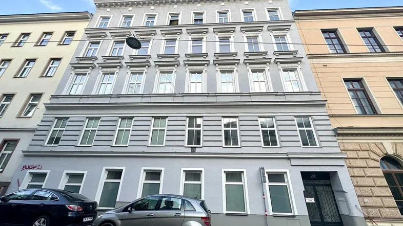 Die Fassade eines mehrstöckigen Wohngebäudes mit vielen Fenstern und geparkten Autos davor.