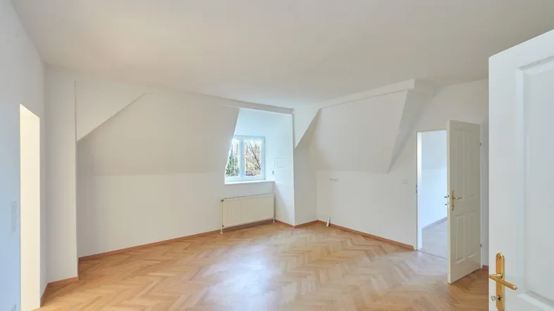 Helles Zimmer im Dachgeschoss mit Parkettboden und schrägen Wänden, bereit zur individuellen Gestaltung.