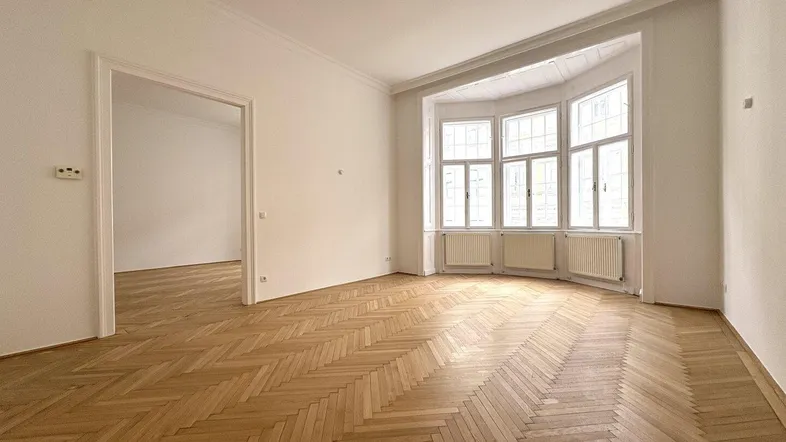 Helles Wohnzimmer mit Fischgrätparkett und einem charakteristischen Erkerfenster, das viel Tageslicht hereinlässt.