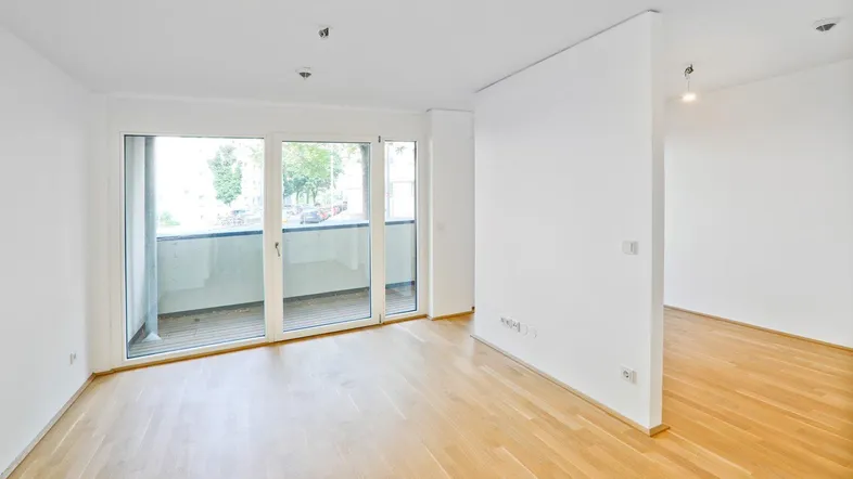 Heller Wohnraum mit Parkettboden und Zugang zu einem Balkon, ideal für offenes Wohnen.