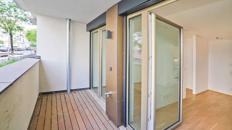 Geräumiger Balkon mit Holzboden und großen Glasfalttüren, die zum hellen Innenbereich führen.