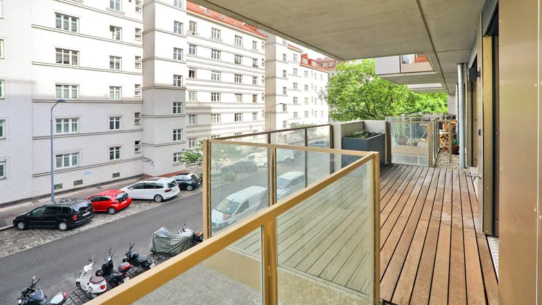 Geräumiger Balkon mit Holzfußboden, Glasgeländer und Blick auf die Straße und umliegende Gebäude.