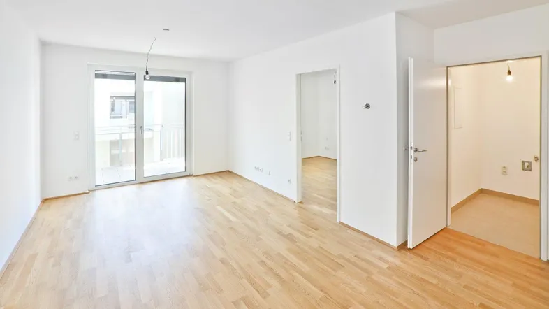 Helles Wohnzimmer mit Parkettboden, großen Fenstern und Zugang zu einem Balkon.