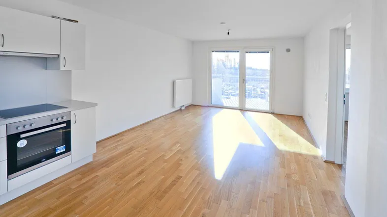 Helles Wohnzimmer mit offener Küche, Parkettboden und Zugang zum Balkon.