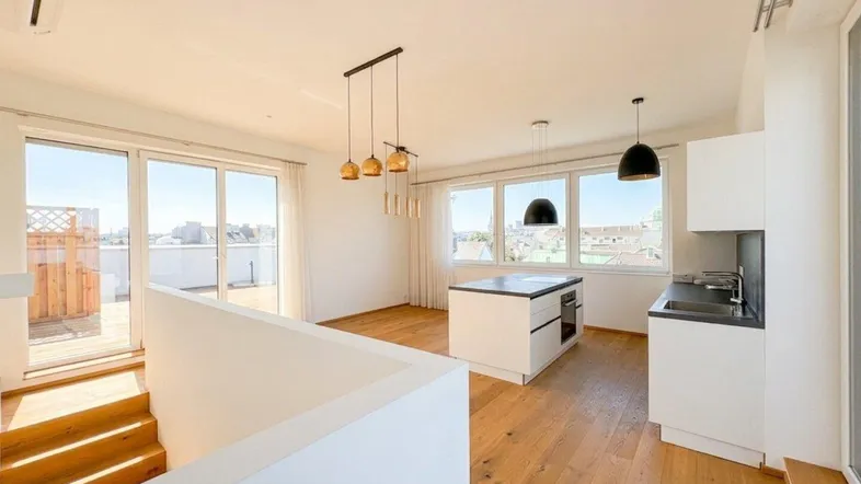 Heller offener Wohn-Essbereich mit moderner Küche, Holzboden und Zugang zu einer Dachterrasse.