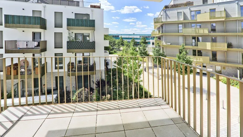 Geräumiger Balkon mit Fliesenboden und Blick auf die moderne Wohnanlage und den begrünten Innenhof.