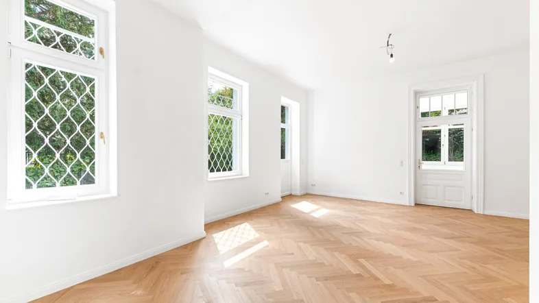 Lichtdurchflutetes Zimmer mit Fischgrätparkett und Fenstern, die viel Tageslicht hereinlassen.