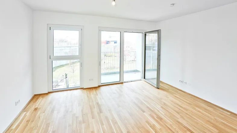 Helles Zimmer mit Parkettboden und Zugang zu einem kleinen Balkon.