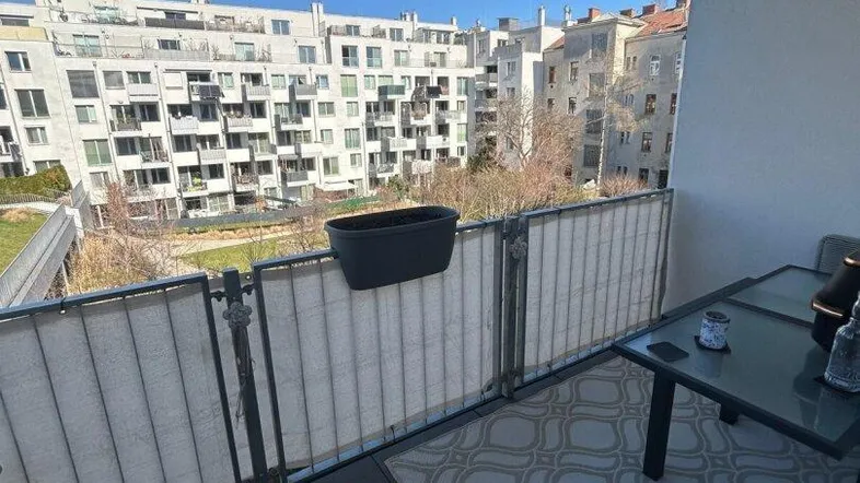 Möblierter Balkon mit Blick auf umliegende Wohngebäude und blauen Himmel.