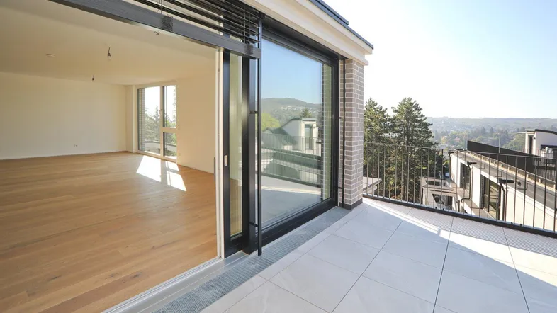 Helles Wohnzimmer mit Holzboden und Schiebetüren, die zu einer großen Terrasse führen und weitem Ausblick.
