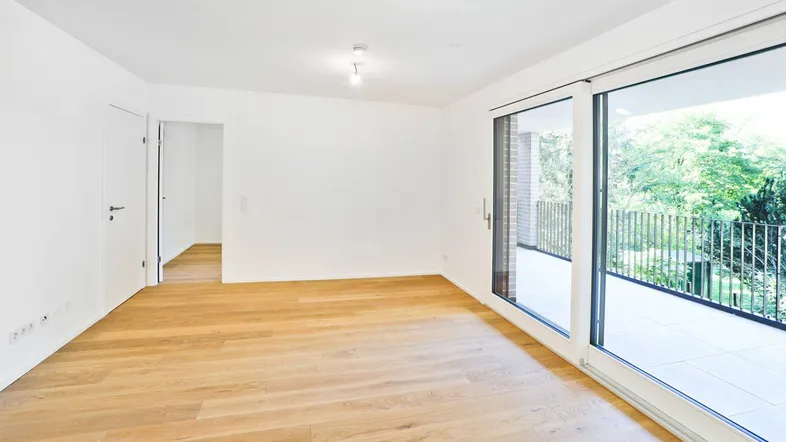 Helles, leeres Zimmer mit Holzboden und großen Schiebetüren zum Balkon.