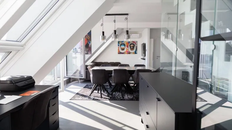 Helles, offenes Wohn- und Esszimmer mit Dachschrägen, großen Fenstern und modernem Arbeitsbereich.