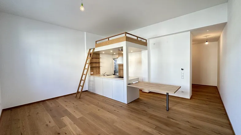 Heller Wohnraum mit integrierter Küchenzeile unter einem Hochbett und schönem Holzfußboden.