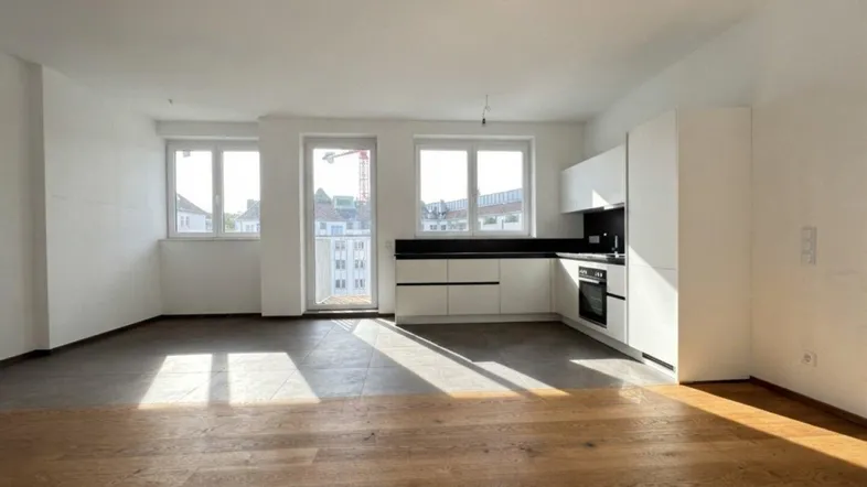 Heller offener Wohn-Essbereich mit moderner Einbauküche, Parkettboden und Zugang zum Balkon.