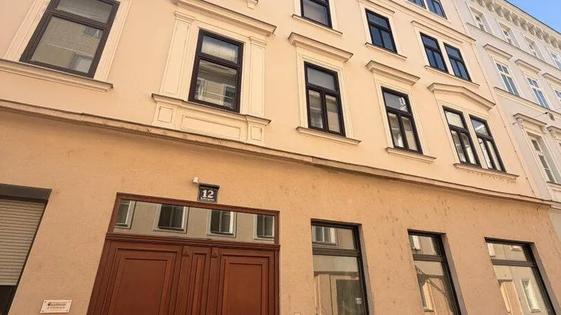 Klassische Fassade eines Mehrfamilienhauses mit braunem Eingangstor und vielen Fenstern.
