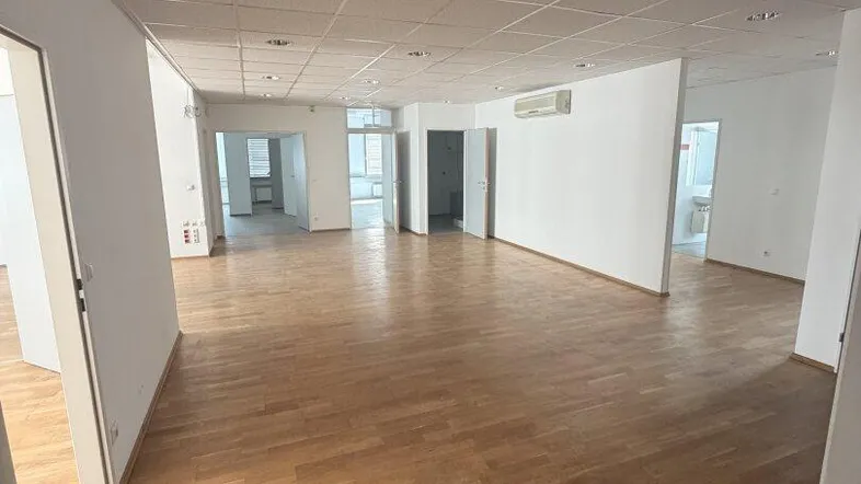 Geräumiger, leerer Büroraum mit hellem Holzparkett und abgehängter Decke, bereit zur individuellen Gestaltung.