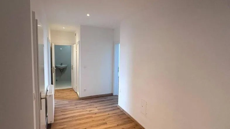 Langer, heller Flur mit Laminatboden, der zu verschiedenen Zimmern und einem Badezimmer führt.