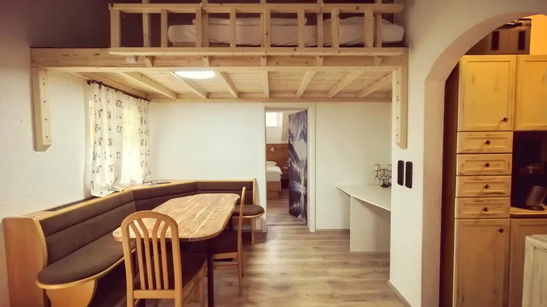 Gemütlicher Wohn-Essbereich mit Holztisch, Eckbank und einem darüberliegenden Schlafbereich im Dachgeschoss.