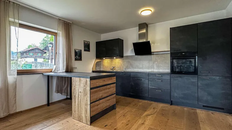 Moderne Küche mit dunklen Schränken, Holzboden und einem Fenster mit Blick ins Grüne.
