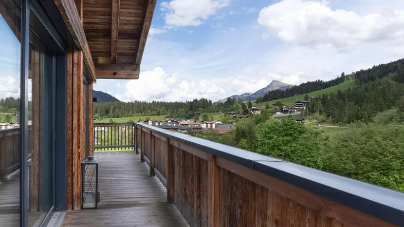 Geräumiger Holzbalkon mit atemberaubendem Blick auf die umliegende Berglandschaft und die Häuser.