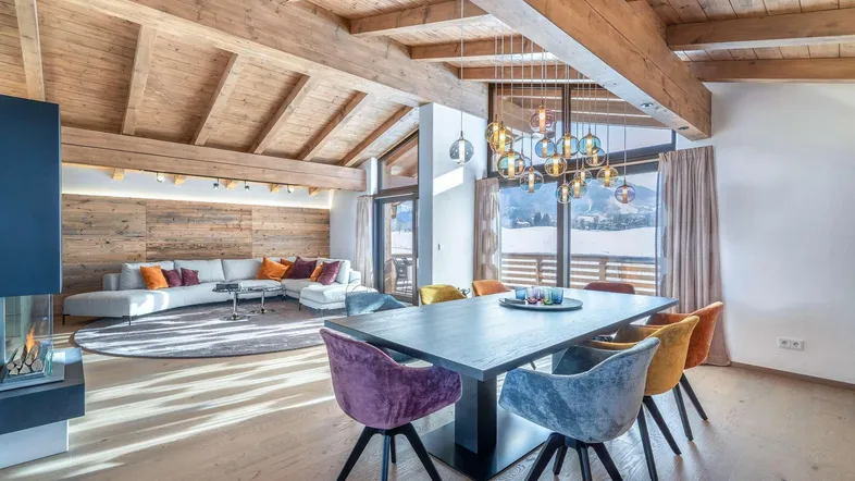 Helles Wohn- und Esszimmer mit Holzbalkendecke, Kamin und Bergblick durch große Fenster.