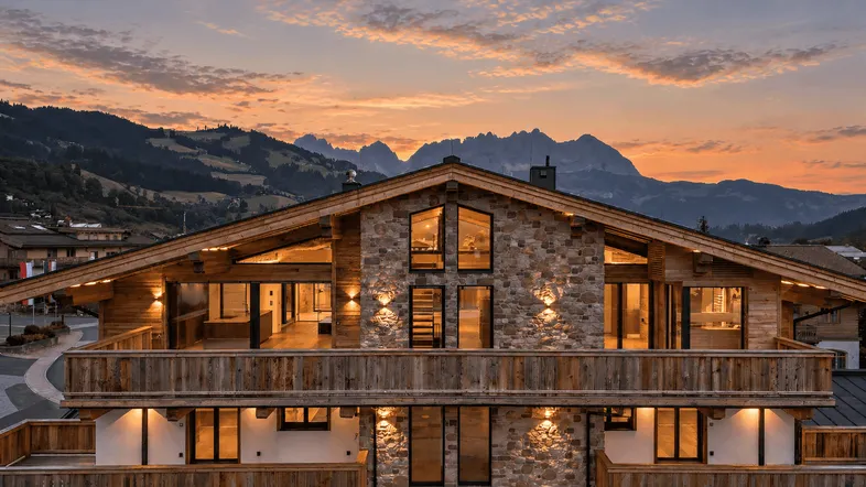 Großzügiges Chalet im alpinen Stil mit Stein- und Holzfassade bei Sonnenuntergang und Bergblick.