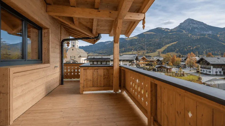Geräumiger Holzbalkon mit traditionellem Geländer und weitem Blick auf die umliegende Berglandschaft und das Dorf.