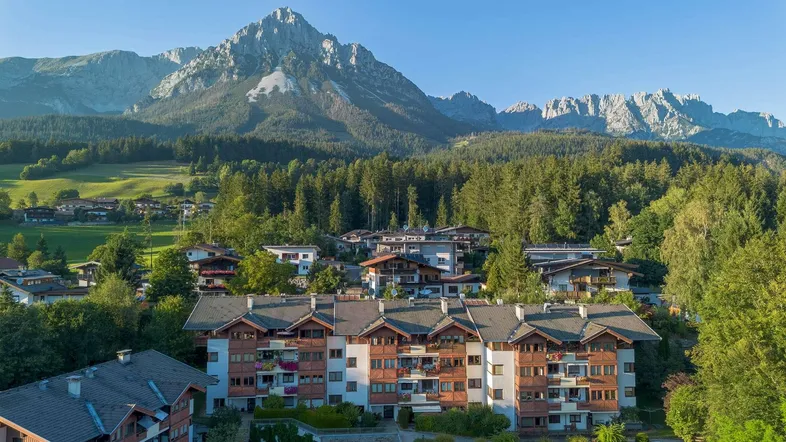 Luftaufnahme von Wohngebäuden in einer malerischen Berglandschaft mit grünen Wäldern.