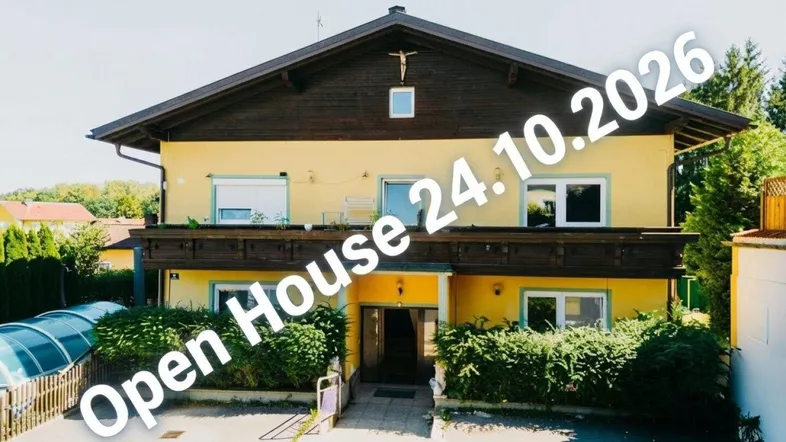 Gelbes Mehrfamilienhaus mit Holzbalkonen und traditionellem Satteldach in sonniger Umgebung.