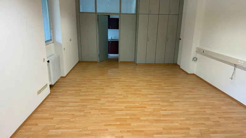 Geräumiger Büroraum mit hellem Laminatboden, weißen Wänden und integrierten Schränken, ideal für verschiedene Nutzungen.