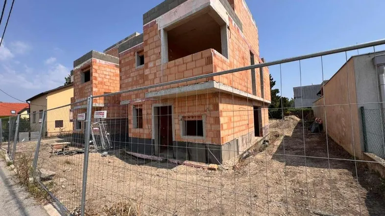 Rohbau eines modernen Hauses mit Ziegelwänden und Betonstrukturen unter blauem Himmel.