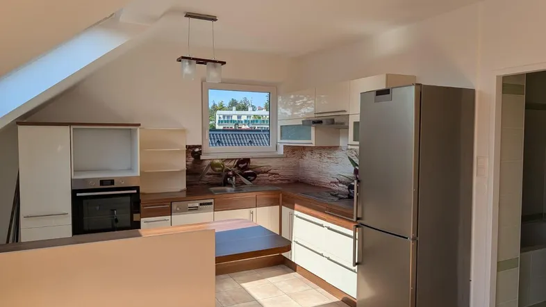 Moderne Küche in Dachgeschosswohnung mit Einbaugeräten, Fliesenboden und Blick nach draußen.