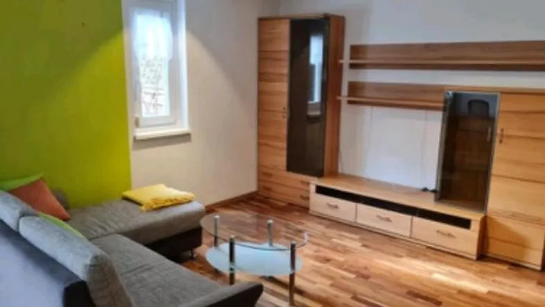 Helles Wohnzimmer mit Holzparkett, grüner Akzentwand und moderner Wohnwand.