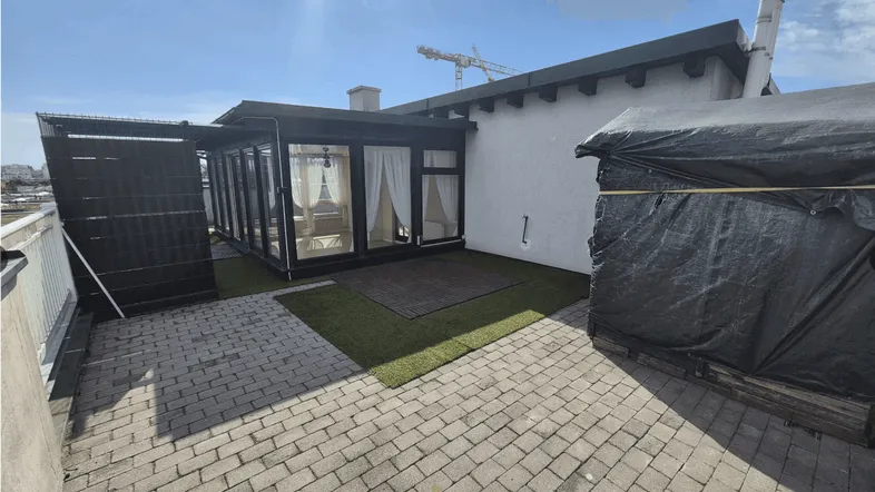 Große Dachterrasse mit Pflastersteinen, Kunstrasen und einem verglasten Wintergartenbereich.