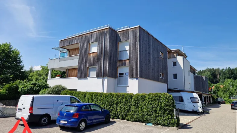 Modernes Mehrfamilienhaus mit Holzfassade, Balkonen und Außenparkplätzen unter blauem Himmel.