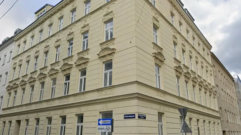 Eckgebäude mit klassischer Fassade und vielen Fenstern an einer städtischen Straße.
