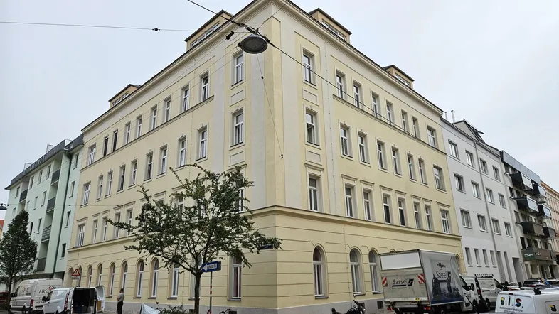Eckgebäude mit gelber Fassade und vielen Fenstern in einer städtischen Umgebung.