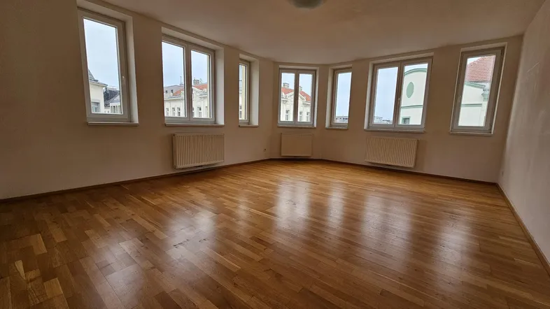 Helles und geräumiges Zimmer mit Parkettboden und vielen Fenstern, die viel Tageslicht hereinlassen.