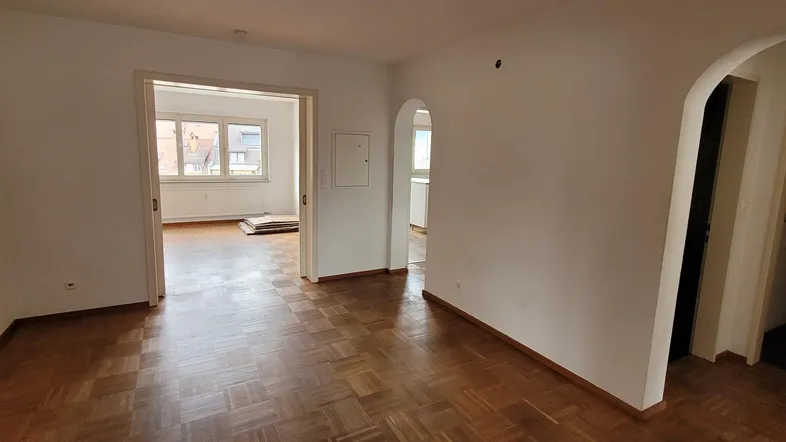 Geräumiges Wohnzimmer mit Parkettboden und mehreren Zugängen zu anderen Räumen.