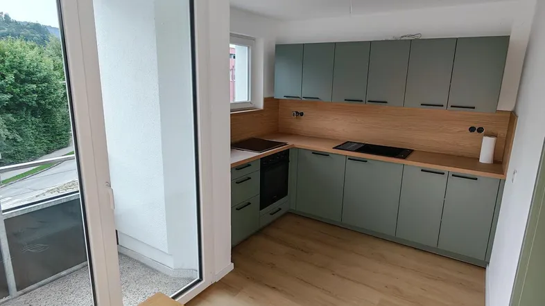 Moderne Küche mit hellgrünen Schränken, Holzarbeitsplatte und Zugang zum Balkon mit Bergblick.